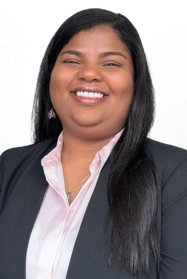 Woman with long straight black hair wearing a black blazer, light pink shirt, and necklace, smiling at the camera against a plain white background.
