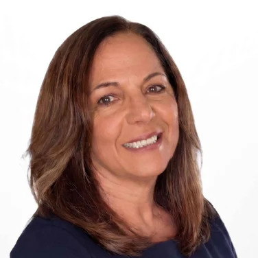 Smiling woman with shoulder-length brown hair, wearing a dark long-sleeve top, poses against a plain white background.