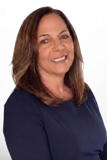 Smiling woman with shoulder-length brown hair, wearing a dark long-sleeve top, poses against a plain white background.