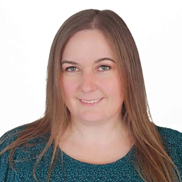 Woman with straight light brown hair wearing a green patterned top, smiling slightly, standing against a plain white background.
