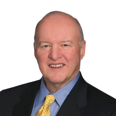 Bald man in a dark suit, blue shirt, and yellow polka dot tie, smiling, posed against a white background.