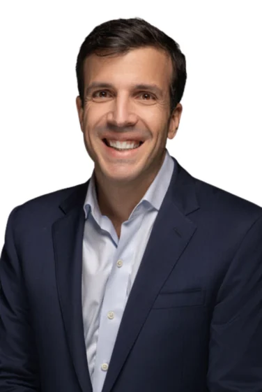 Man in a navy suit jacket and light blue shirt smiling at the camera against a white background.