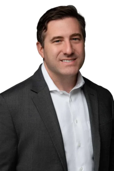 Man with short brown hair wearing a dark suit jacket and white dress shirt, smiling slightly, posed in front of a plain white background.