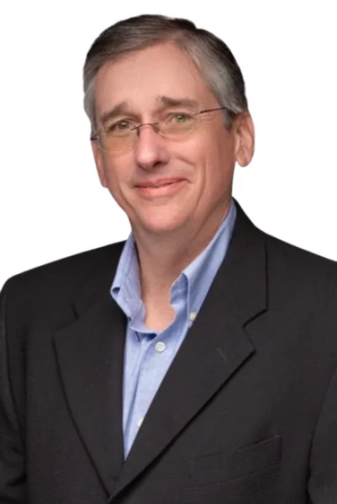 A middle-aged man wearing glasses, a blue button-up shirt, and a black blazer poses against a white background.
