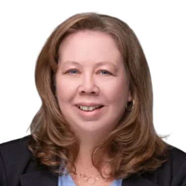 Woman with shoulder-length light brown hair wearing a black blazer and light blue blouse, smiling at the camera against a plain white background.