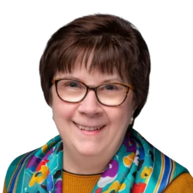 Smiling woman with short brown hair, glasses, and a colorful floral scarf over a mustard yellow top, against a white background.