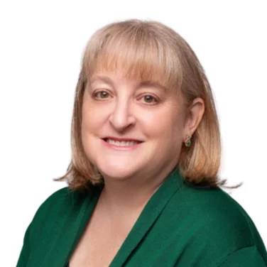 Woman with shoulder-length blonde hair, wearing a green cardigan and black top, smiling at the camera against a white background.
