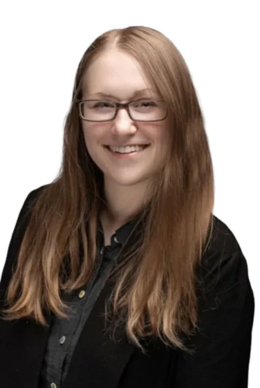 A person with long light brown hair and glasses is smiling, wearing a black blazer over a dark shirt, against a white background.