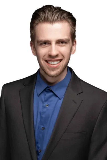 Smiling young man with short brown hair wearing a dark blazer and blue dress shirt, photographed against a white background.