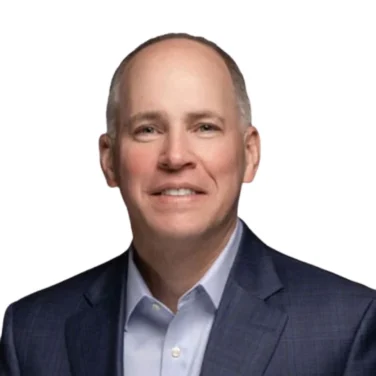 A middle-aged man in a blue suit jacket and light blue shirt smiles at the camera against a plain white background.