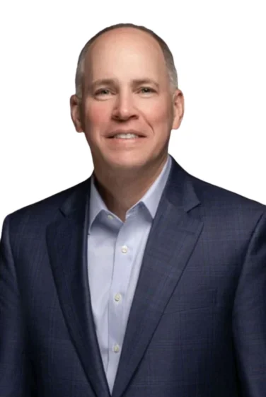 A middle-aged man in a blue suit jacket and light blue shirt smiles at the camera against a plain white background.