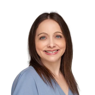 Woman with straight brown hair wearing a light blue blouse, smiling and posing against a plain white background.