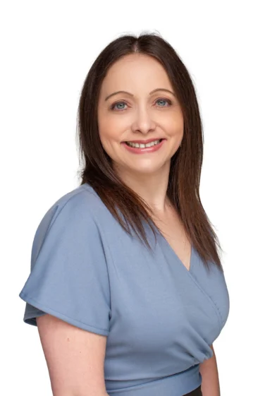 Woman with straight brown hair wearing a light blue blouse, smiling and posing against a plain white background.