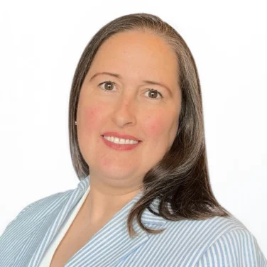 Woman with long brown hair wearing a light blue and white striped blazer over a white top, smiling at the camera against a plain white background.