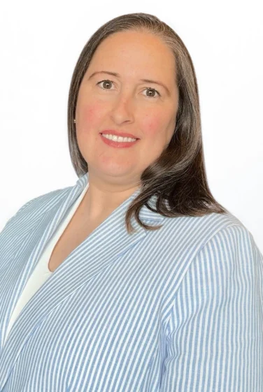 Woman with long brown hair wearing a light blue and white striped blazer over a white top, smiling at the camera against a plain white background.