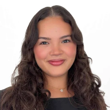 A woman with wavy dark hair and a black top smiles at the camera against a white background.