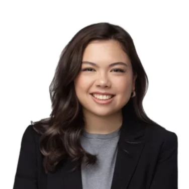 Woman with long dark hair wearing a black blazer and grey shirt, smiling with arms crossed, isolated on a white background.