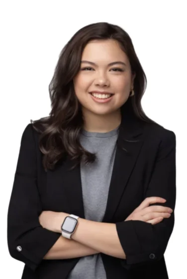 Woman with long dark hair wearing a black blazer and grey shirt, smiling with arms crossed, isolated on a white background.