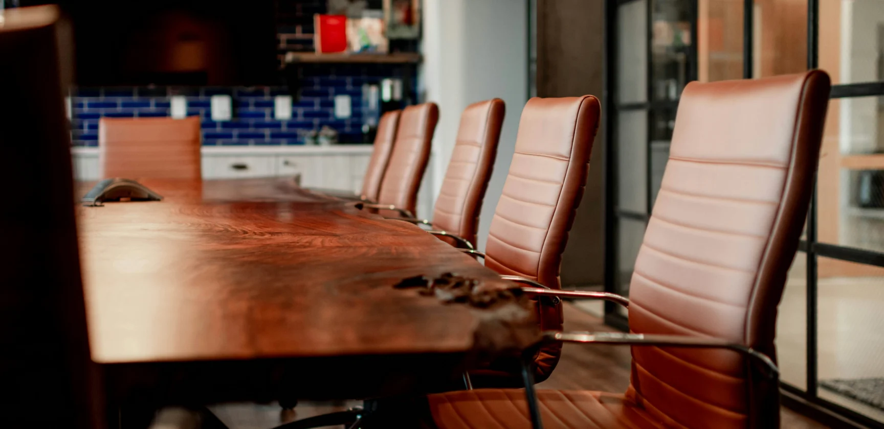 A row of brown leather chairs lines one side of a wooden conference table in a modern office meeting room.