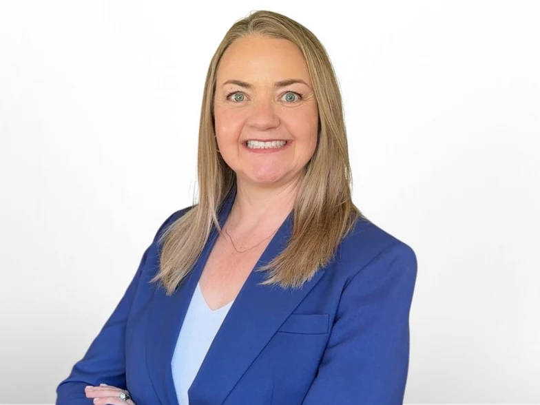 A smiling woman with shoulder-length blonde hair wearing a blue blazer over a light shirt.