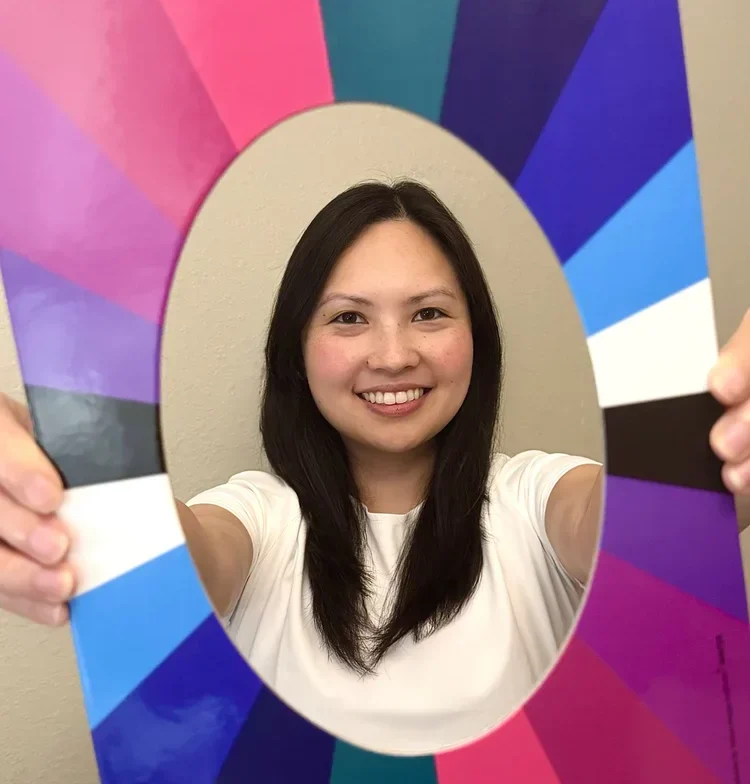 A woman holds an oval-shaped frame printed with a colorful, radial spectrum of blue, purple, and pink segments around her face.